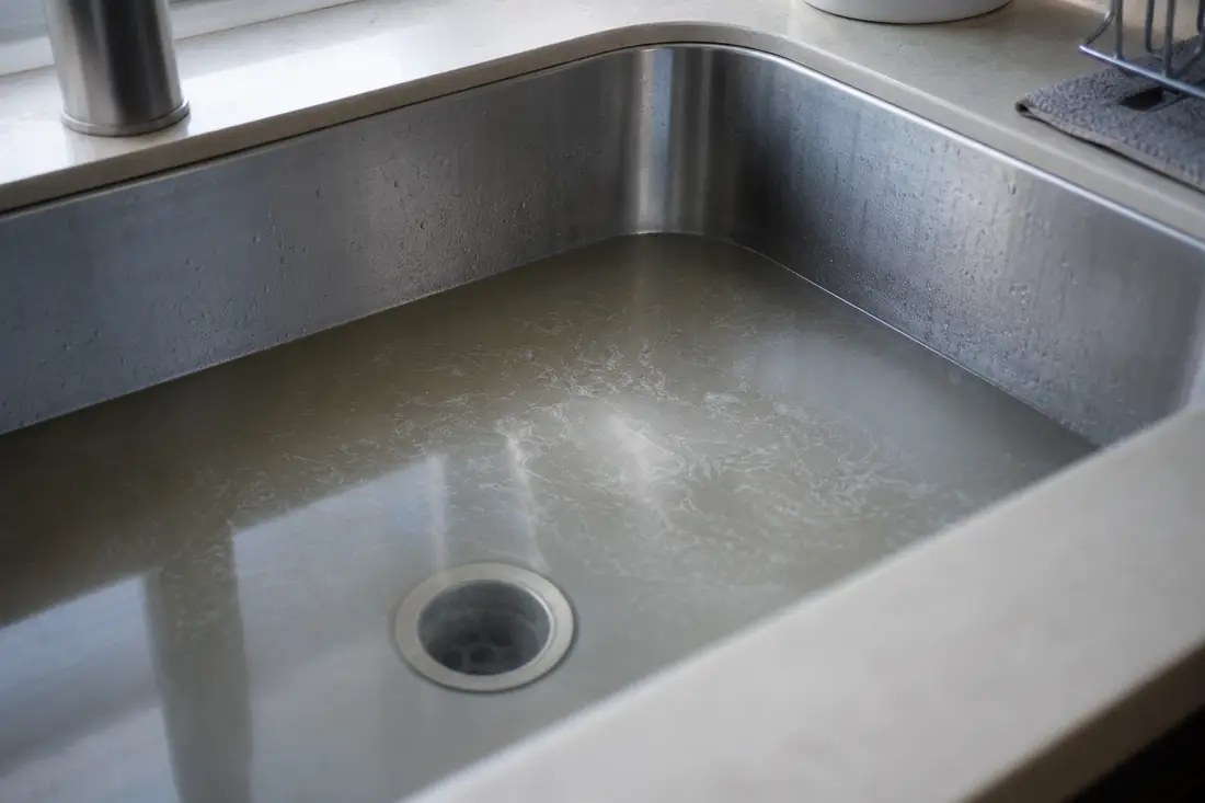 Évier de cuisine rempli d'eau stagnante à cause d'une canalisation bouchée, dans un logement de Suisse romande